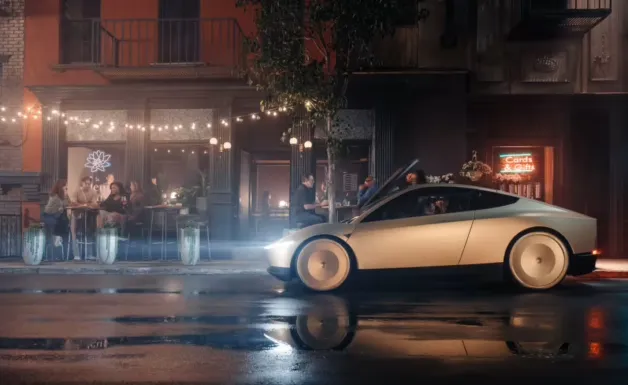 image-1750997477583-2316.webp Elon Musk dan logo Tesla di latar belakang pabrik kendaraan listrik