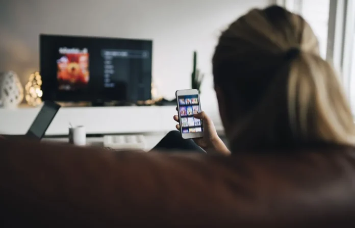 image-1753589441858-6658.webp Orang menggunakan smartphone sambil menonton TV di ruang keluarga