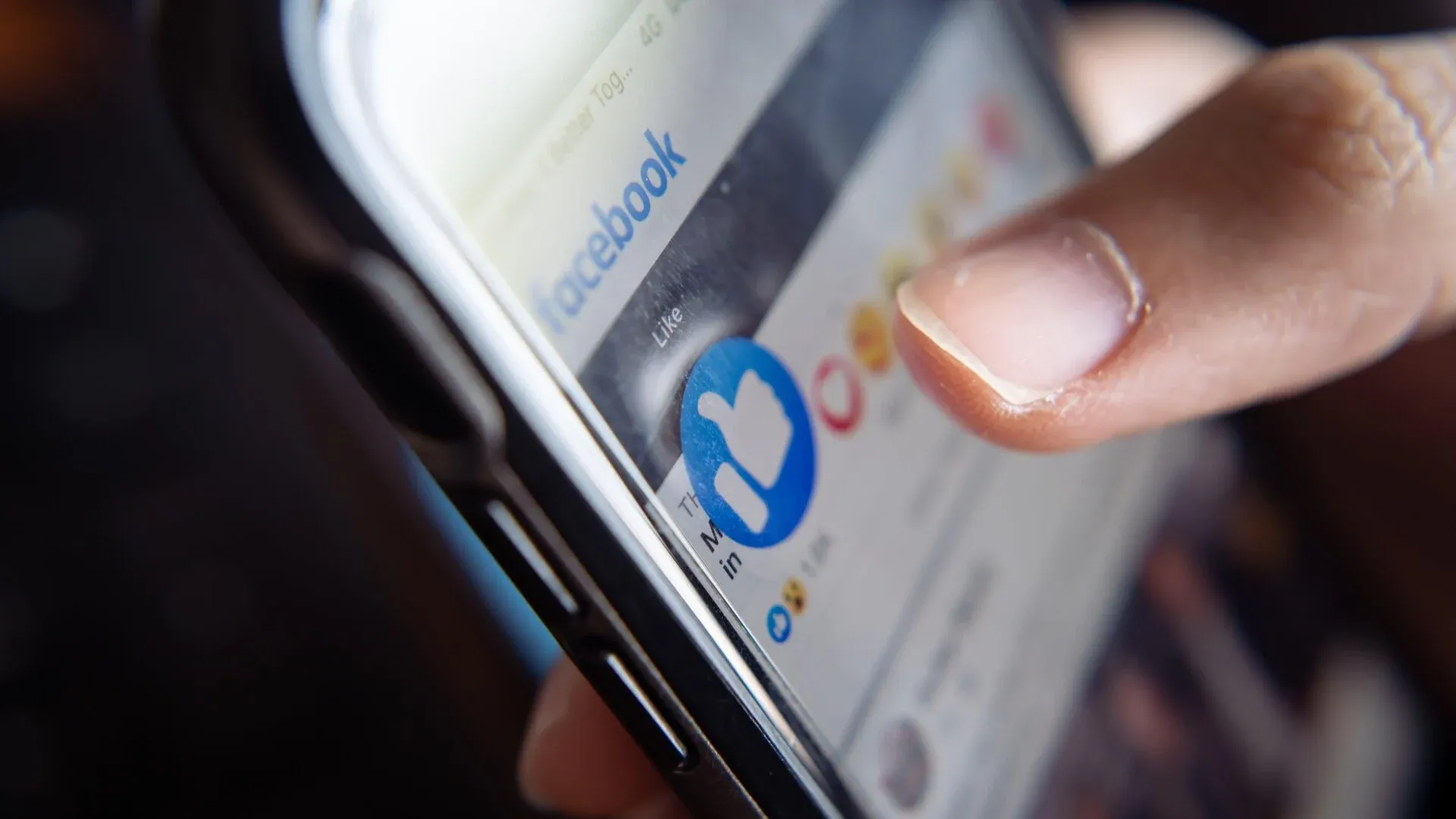 Facebook is displayed on a smartphone, with a person's hand tapping to like a post.