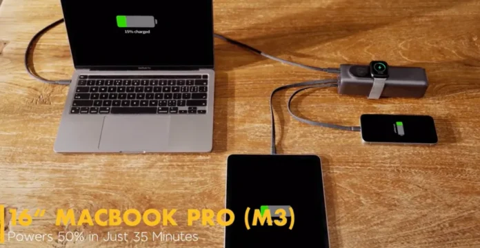 Power bank Ampsos 5-in-1 berwarna hitam dengan layar OLED kecil yang menampilkan status baterai, diletakkan di atas meja kayu