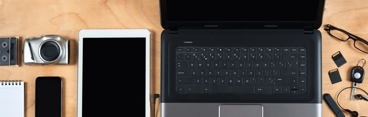 Electronics and gadgets organized on a wooden surface including a laptop tablet camera smartphone and accessories